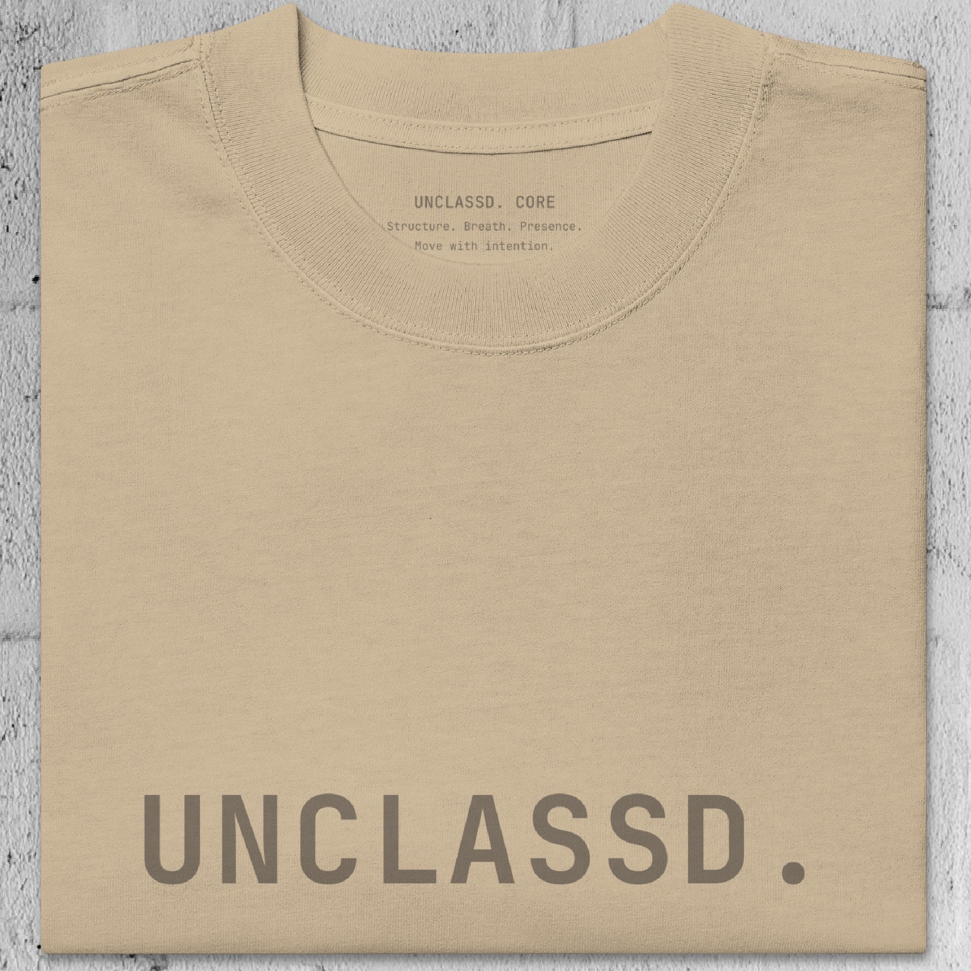 Close-up of faded khaki/beige heavyweight 240gsm cotton texture from the UNCLASSD CORE Oversized Tee, garment-dyed surface.