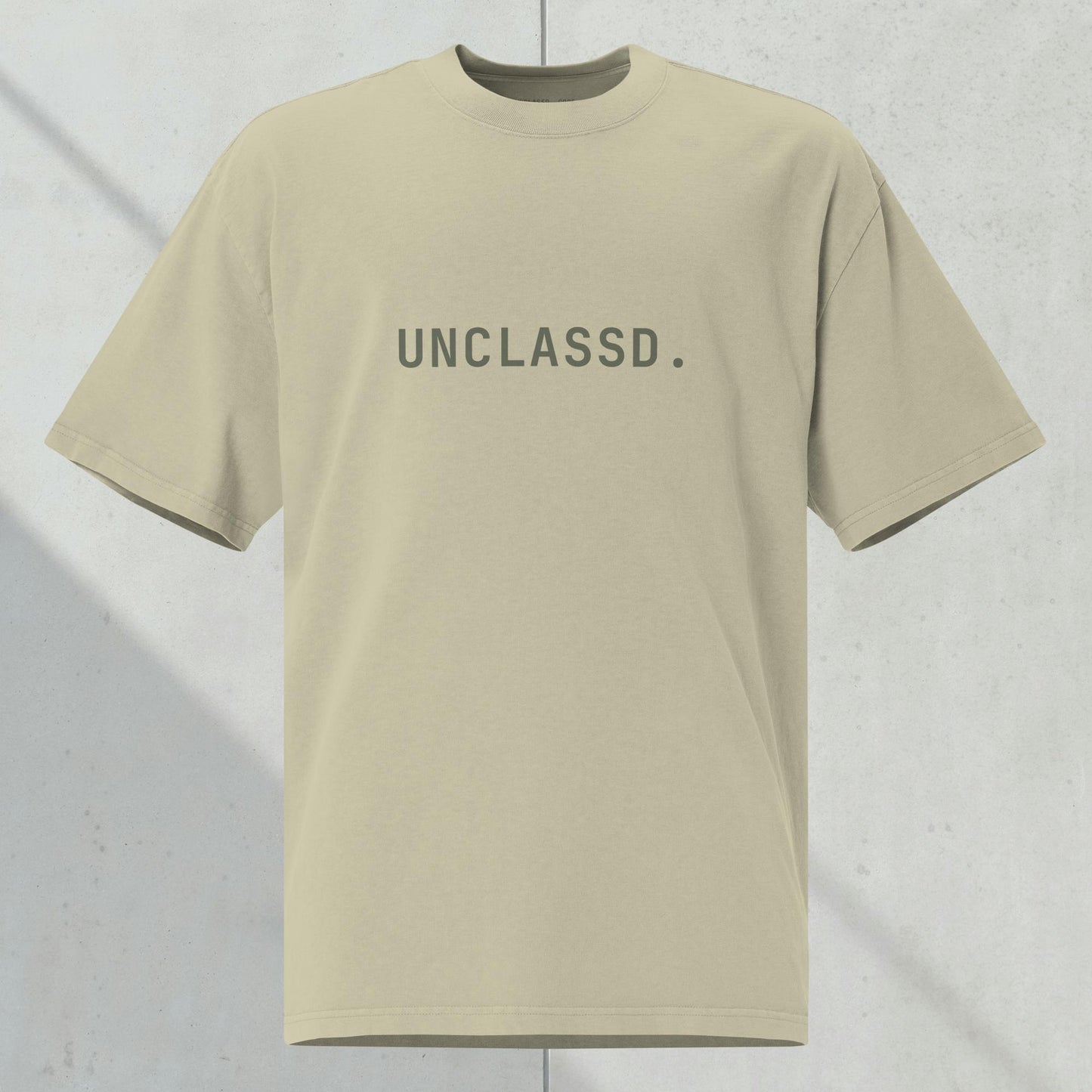 UNCLASSD CORE Oversized Tee in faded eucalyptus /sage with tonal “UNCLASSD.” chest print, ghost mockup against  concrete background.